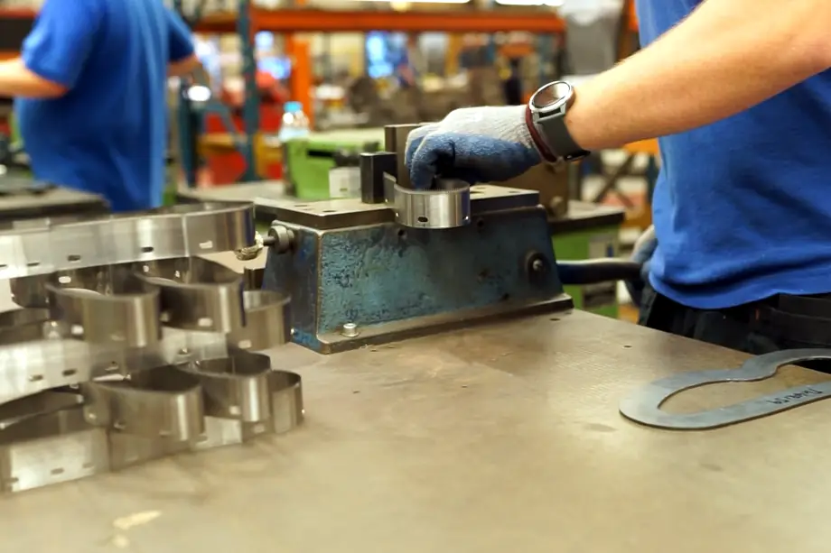 An engineer, manually bending a strip of stainless steel to exactly fit a pre-made jig