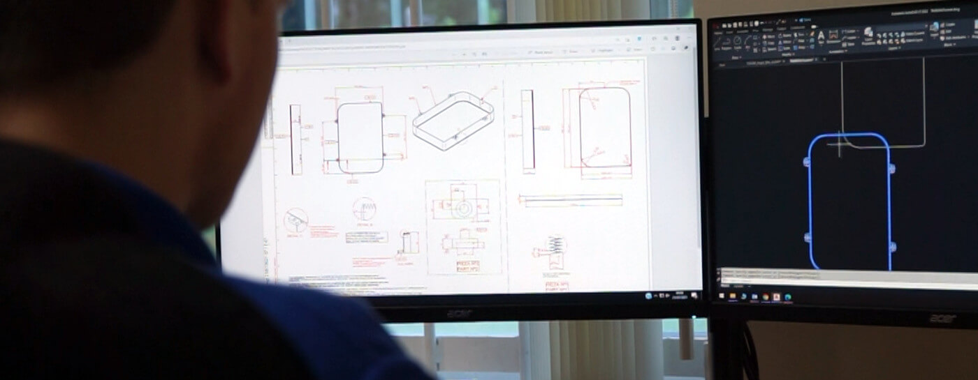 Computer aided design technician drawing a bespoke tray knife design on a dual monitor computer.